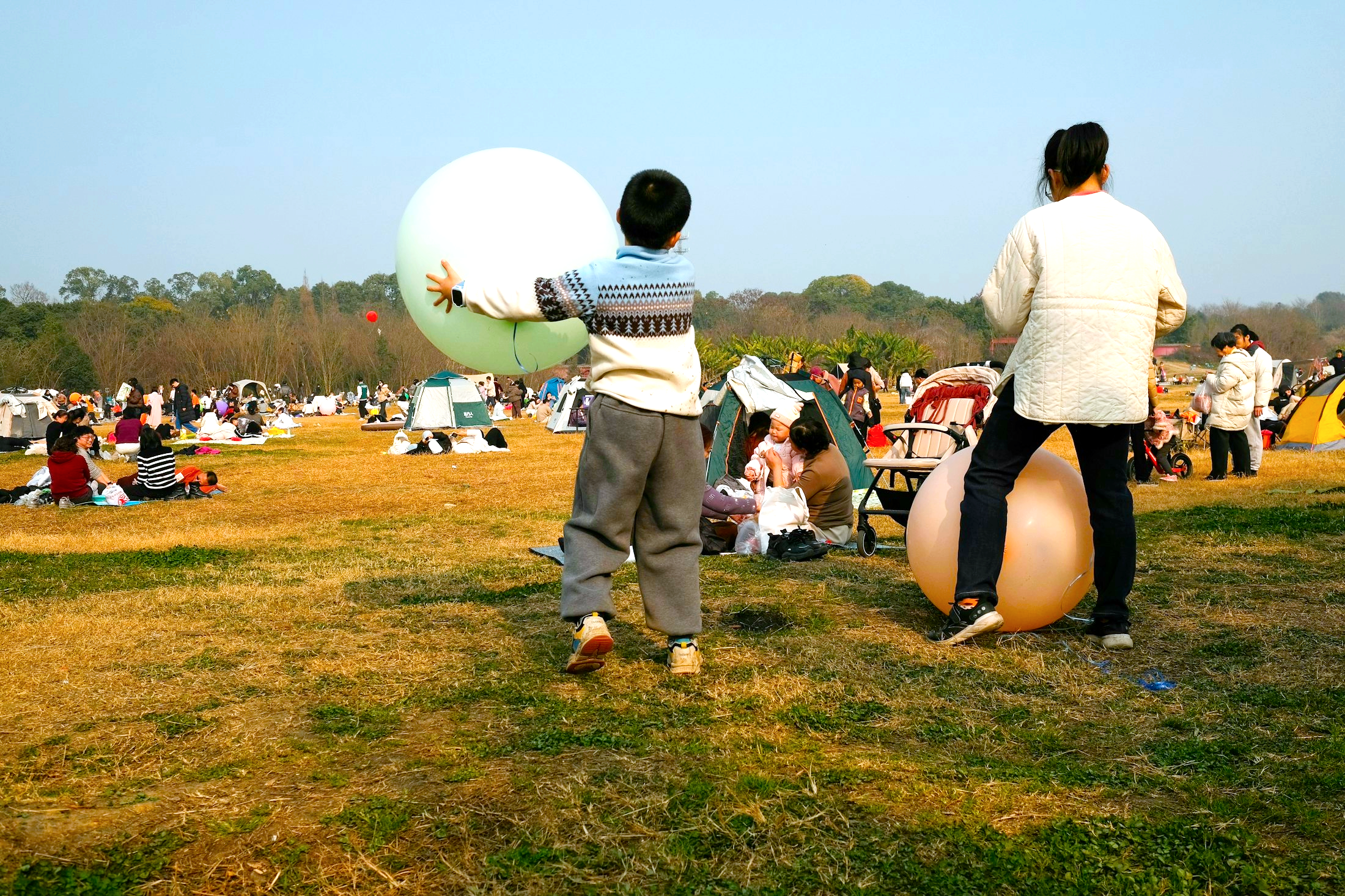 Families gathered in a park for an outdoor community event with children holding large balloons.