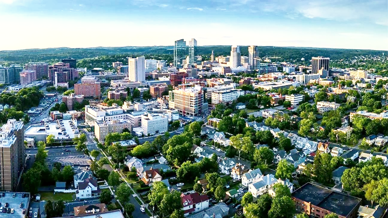 Aerial view across White Plains with downtown towers rising above nearby homes and tree-lined streets.