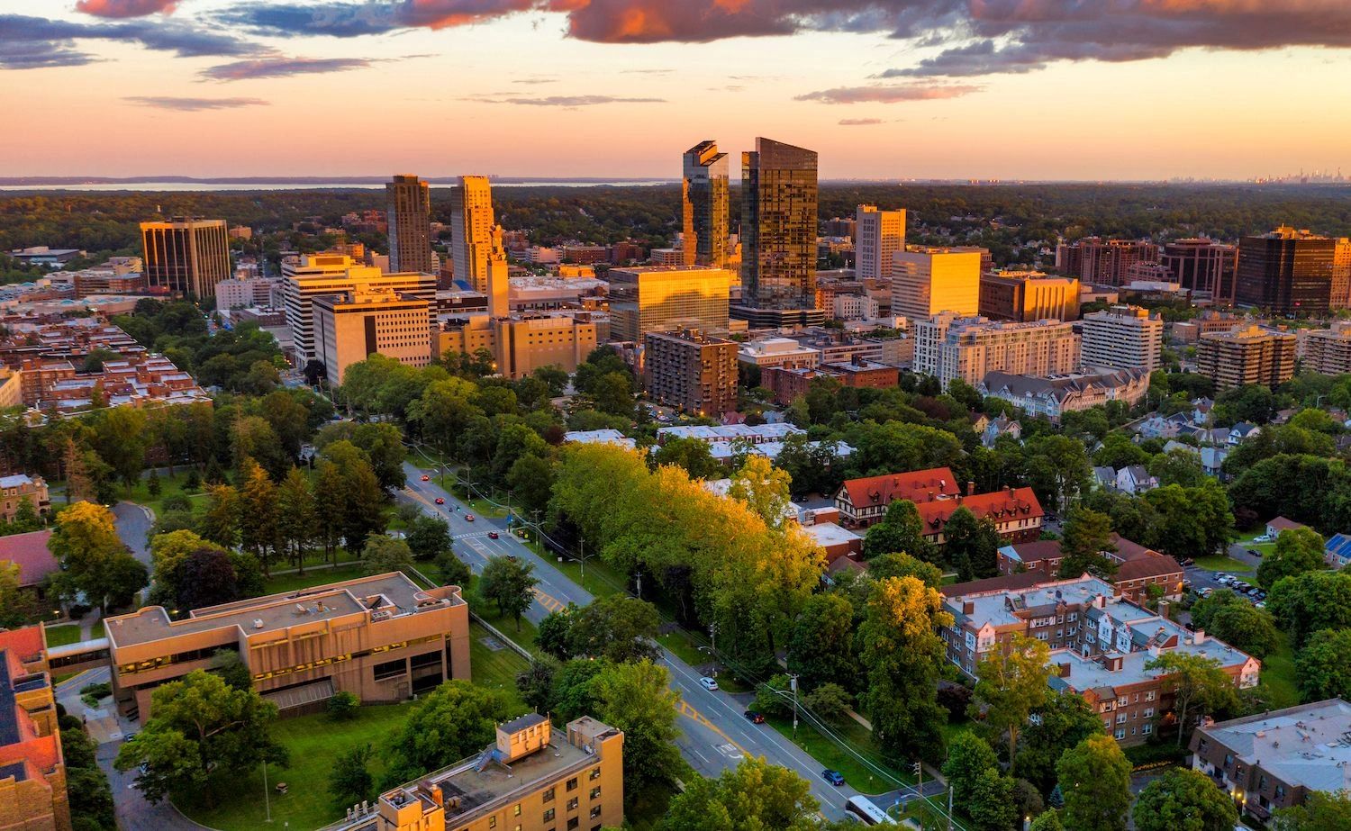 Golden-hour aerial view of downtown White Plains with neighborhoods, treetops, and streets stretching toward the horizon.