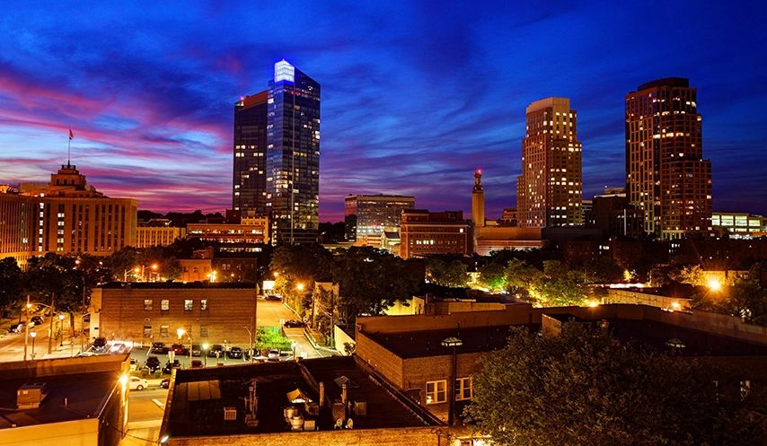 Downtown White Plains at twilight with office towers, apartment buildings, and the city skyline lit against a deep blue sky.
